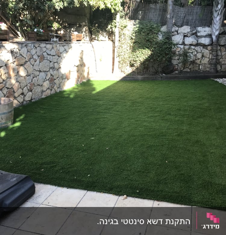 דשא סינתטי בגינה עם עציצים על קיר אבן